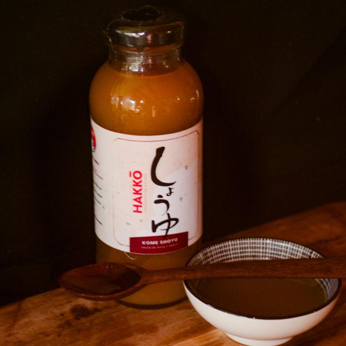 botella de salsa Kome Shoyu y bowl con la salsa y cuchara de madera con fondo negro